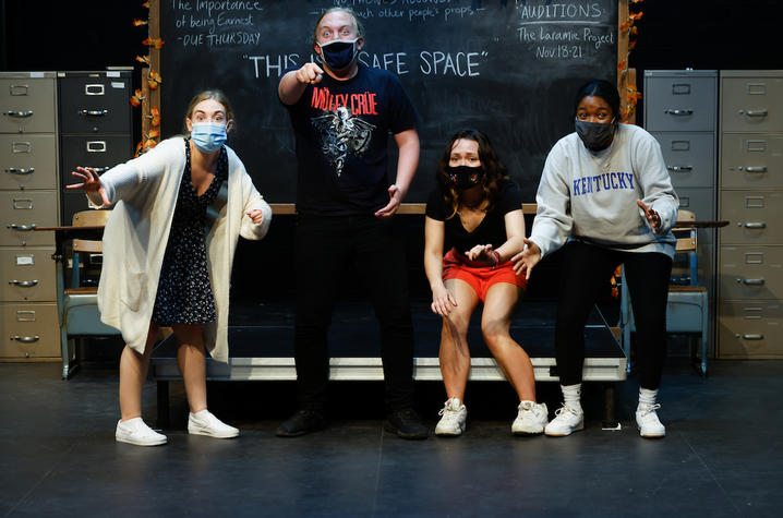 Four students in funny poses in front of blackboard on stage