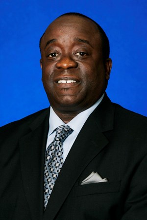 headshot of man in suit with blue tie and in front of blue background