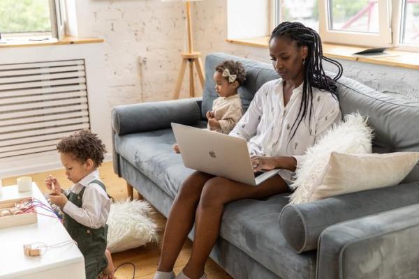 photo of woman sitting on couch with two children playing