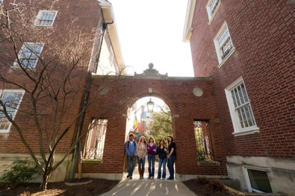 five students standing under archway of brick building