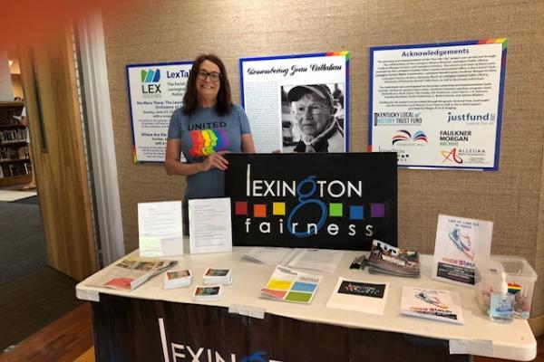 woman standing with poster board reading Lexington Fairness with rainbow colors