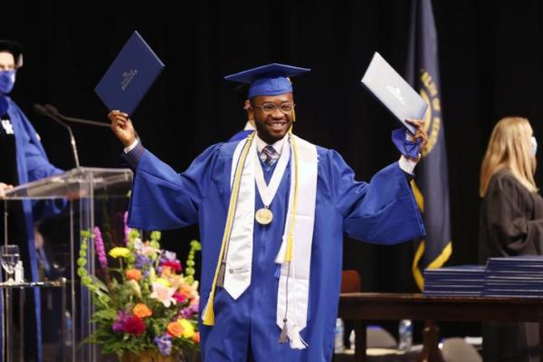 Student wearing cap and gown holding diplomas on graduation stage