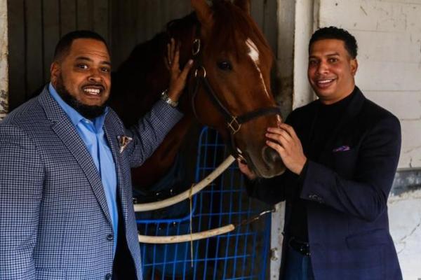 two black men smiling at camera while petting horse
