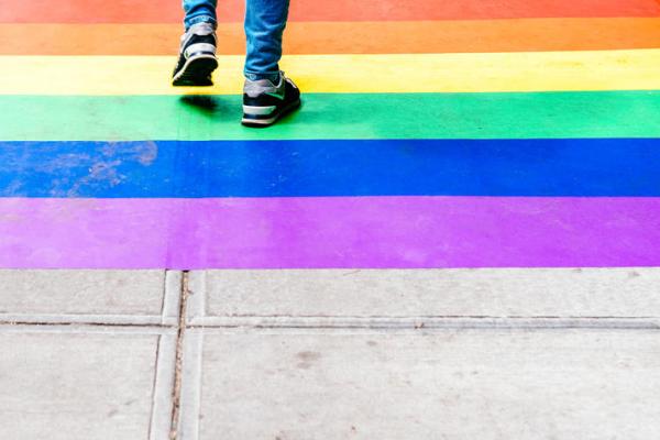 shoes of pedestrian walking on rainbow painted sidewalk
