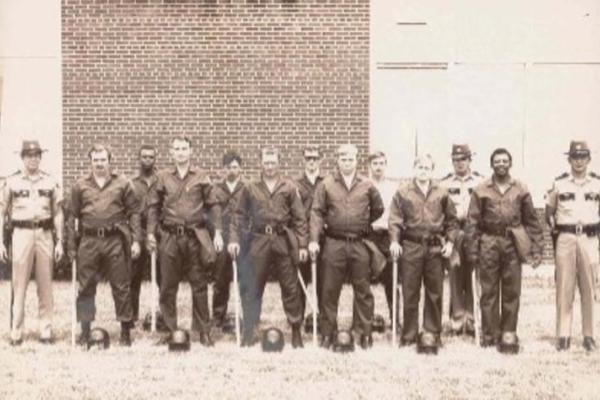sepia toned photo of thirteen officers, including the first Black campus police officer