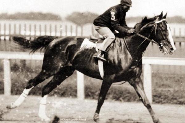 Image in black and white of a Black male jockey racing a horse
