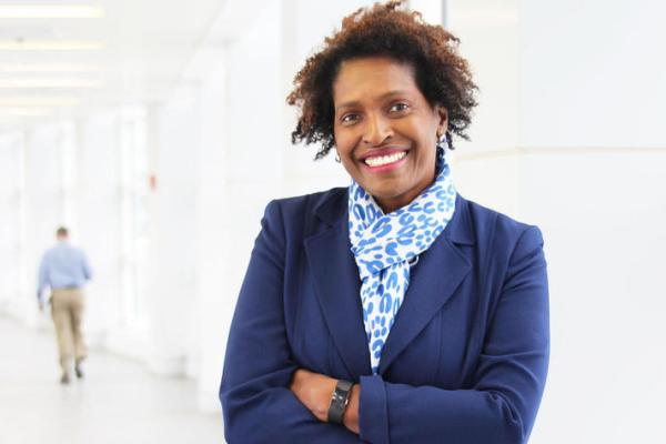 woman in navy suit jacket and light blue scarf smiling for headshot inside building