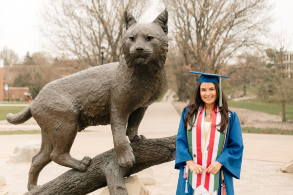 Woman in graduation regalia smiling in front of wildcat statue