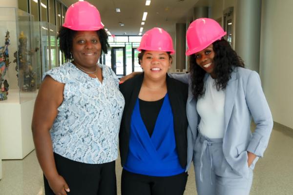 Three women posing for a photo with pink hard hats on. 