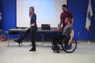 woman demonstrating leg lift exercise to man in wheelchair
