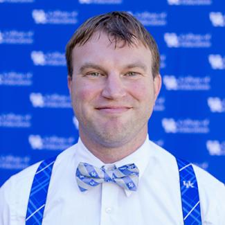 headshot of man wearing University of Kentucky suspenders, white button up, and blue and gray bowtie