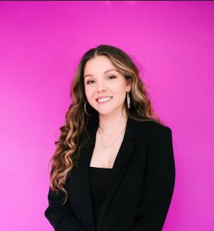 woman standing in front of pink wall wearing black blazer and black blouse
